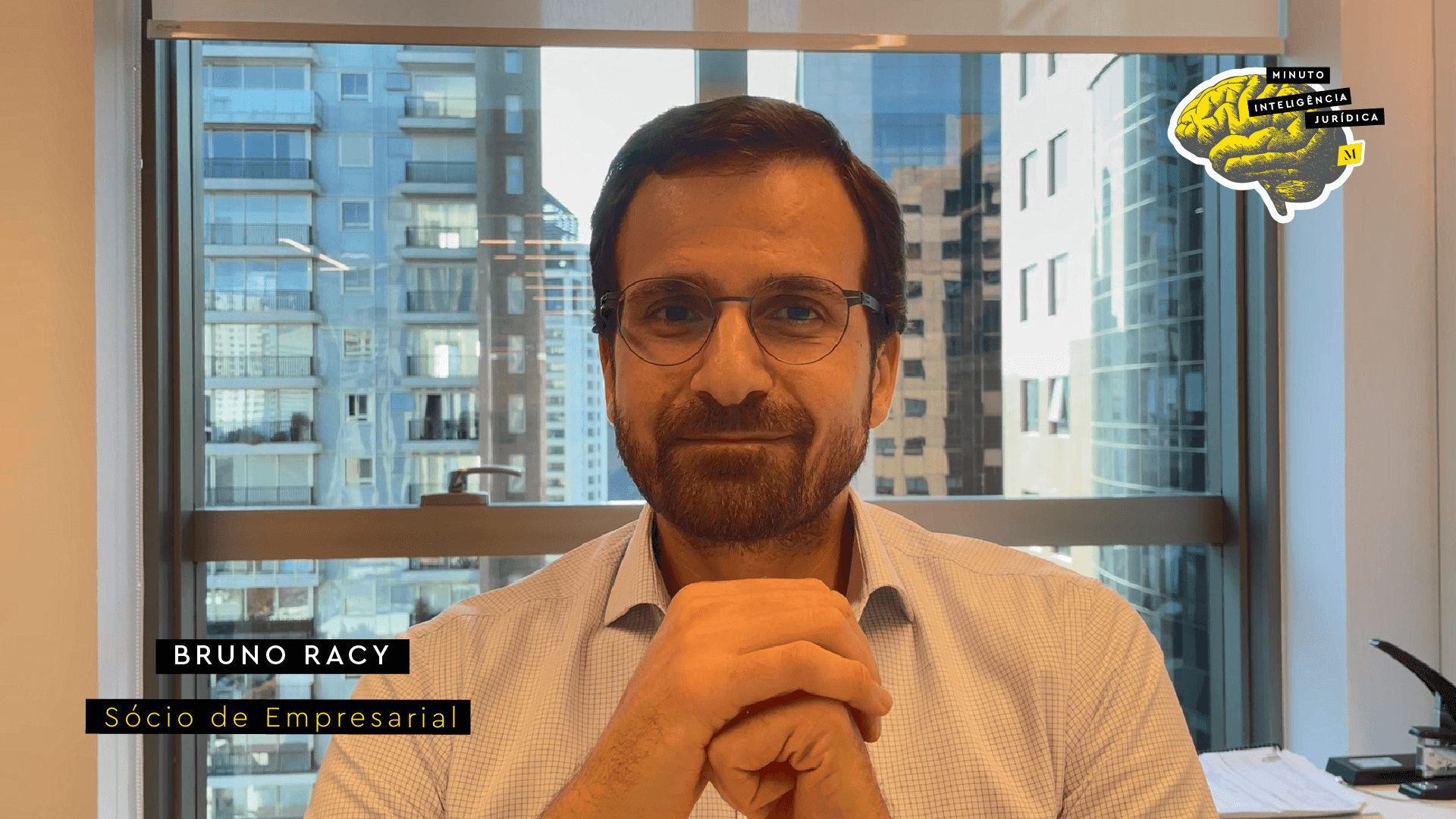 Homem branco com barba, usando camisa social clara e óculos de grau, com as mãos cruzadas. No canto inferior esquerdo, os dizeres: Bruno Racy - Sócio de Empresarial. No canto superior direito, desenho de um cérebro amarelo, usado como logotipo do Portal Inteligência Jurídica
