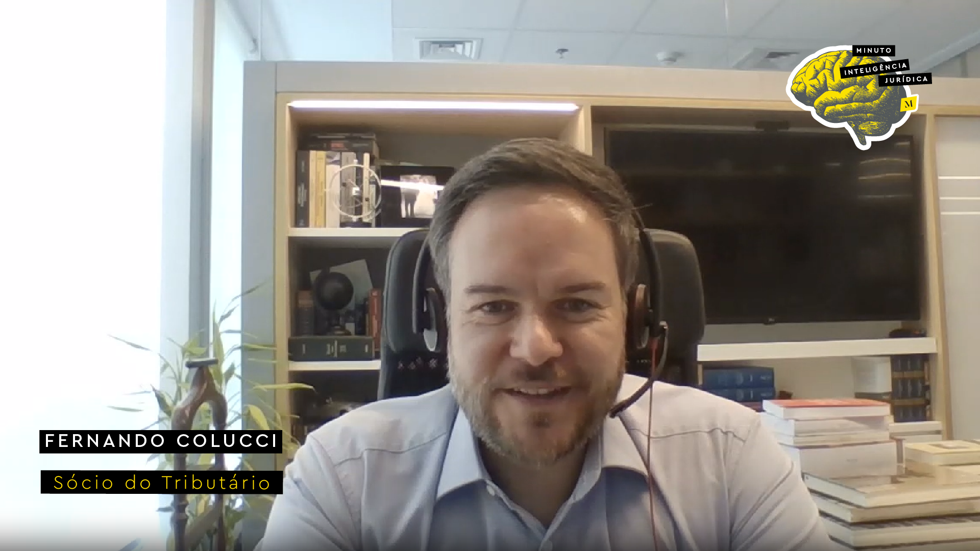 Homem olhando para a foto e sorrindo, usando camisa cinza e headset preto com fio vermelho. No canto inferior esquerdo, frase com os dizeres "Fernando Colucci - sócio do Tributário". No canto superior direito, logotipo do Inteligência Jurídica