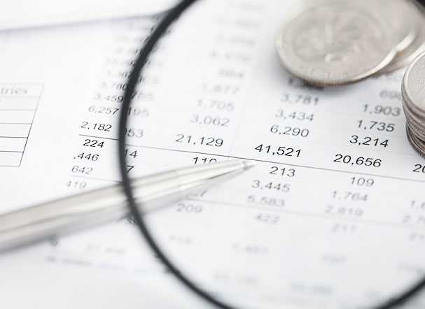 Magnifying glass focusing on a pile of silver coins. Below the coins, a sheet of white sulphite paper with several numbers printed on it