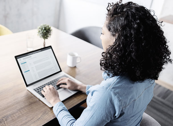 Woman on her back, wearing a blue shirt and with short curly hair, typing on a laptop