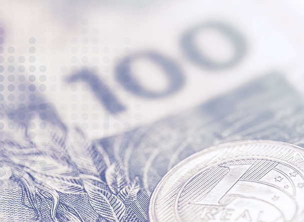 Moeda de um real em cima de uma nota de cem reais