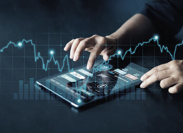 A white person is typing on a tablet positioned on a gray table. On the tablet's screen is information about the financial market