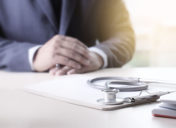 Beige clipboard with white sulphite sheet and stethoscope above, positioned on a table.