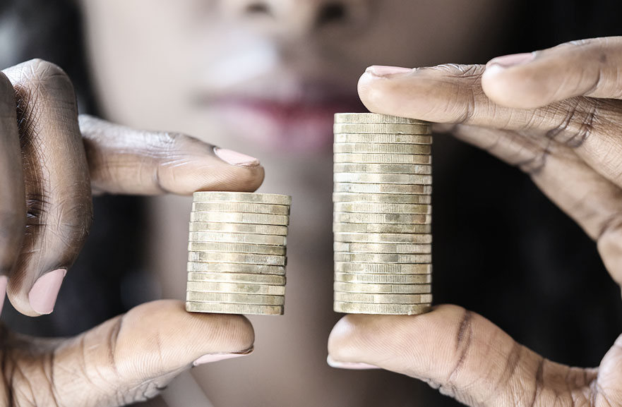 Mulher negra segurando dois montes de moeda. Na mão esquerda, as moedas são em menor número, enquanto na mão direita, são em maior número